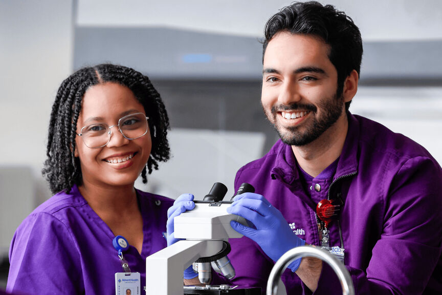 a male and a female medical lab science student practicing microscope skills in a lab