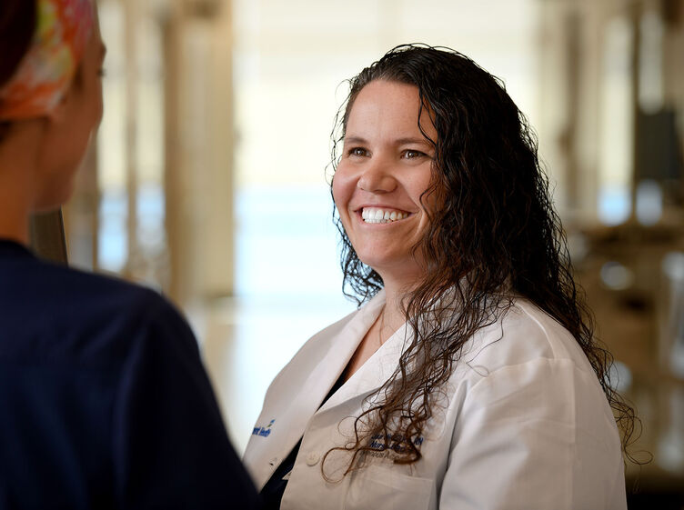 A nurse in a white coat smiling and talking with another nurse