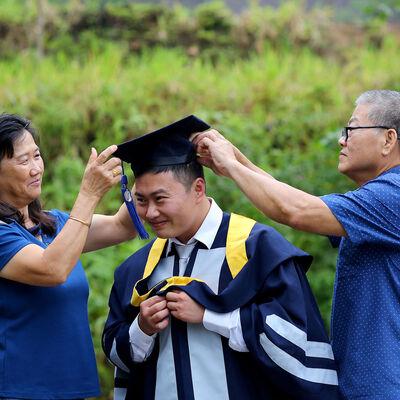 Parents help a graduate get dressed in cap and gown