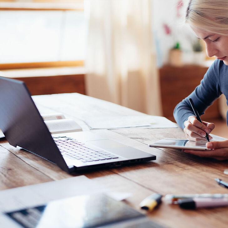 A Woman Writes on Her Tablet at Her Desk