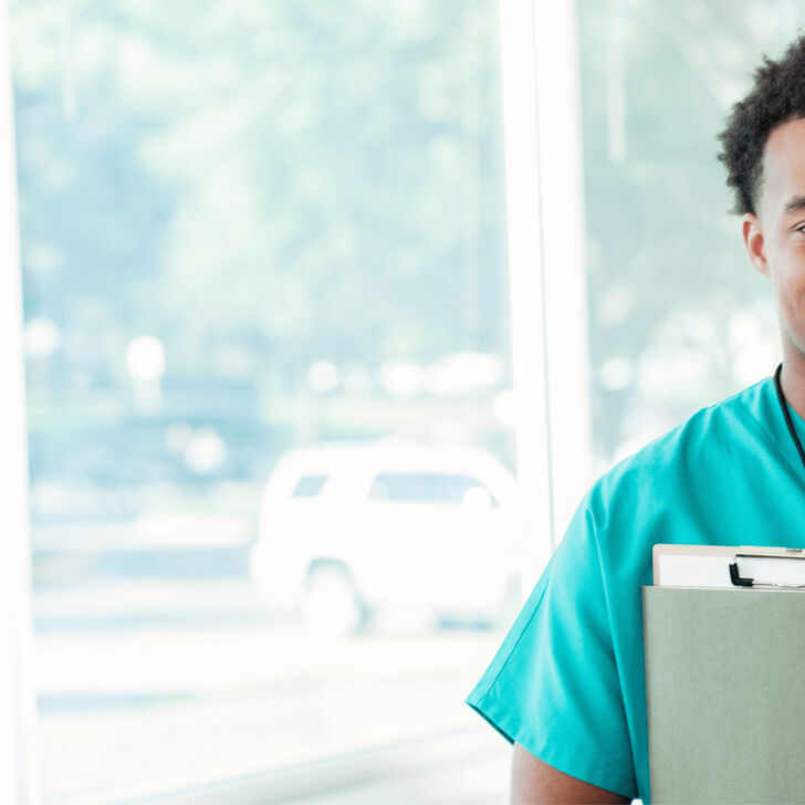 A smiling Male nurse holding a clipboard.