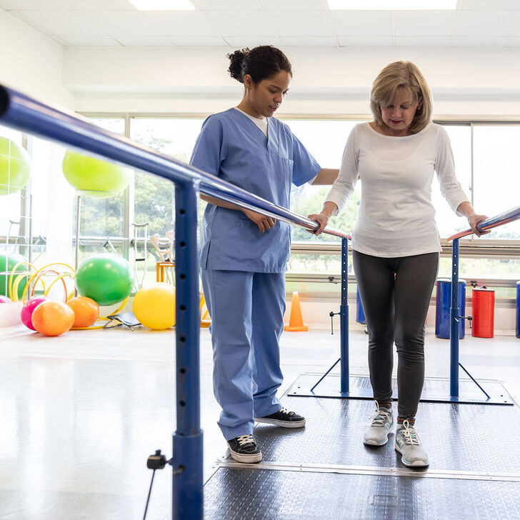 A physical therapist works with a patient who is using parallel bars