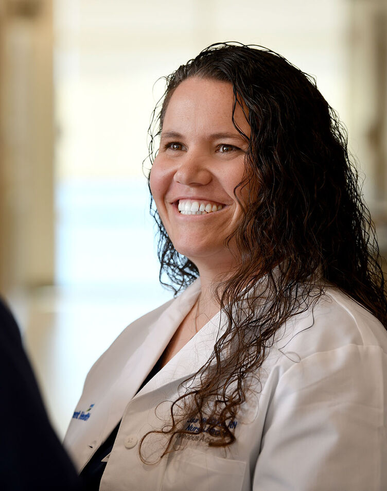 A nurse in a white coat smiling and talking with another nurse