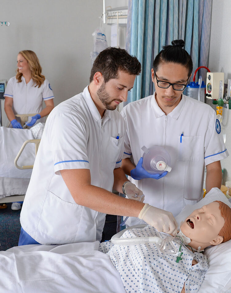 Two nursing students practice their skills in the lab using a patient simulator